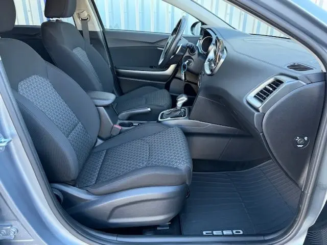 Intérieur avant droit de la Kia CEE'D argent lunaire 2024, sièges tissu noir et console centrale avec boîte auto.