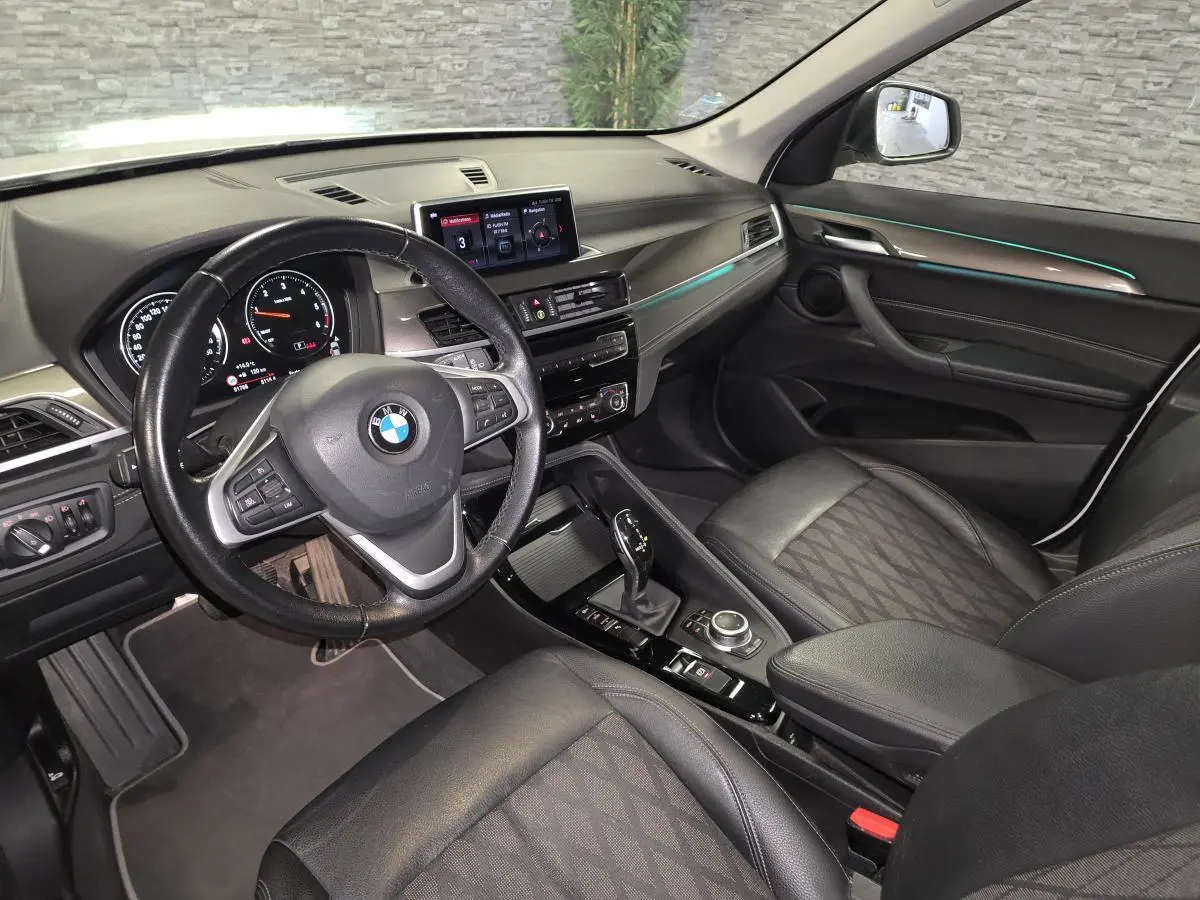 Vue intérieure côté conducteur du BMW X1 sDrive 18d 2022, sellerie cuir tissu noire avec éclairage d'ambiance bleu.