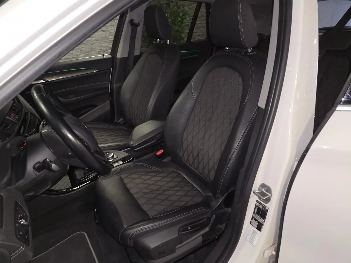 Vue intérieure côté conducteur du BMW X1 blanc 2022, sièges avant en cuir et tissu avec surpiqûres contrastantes.