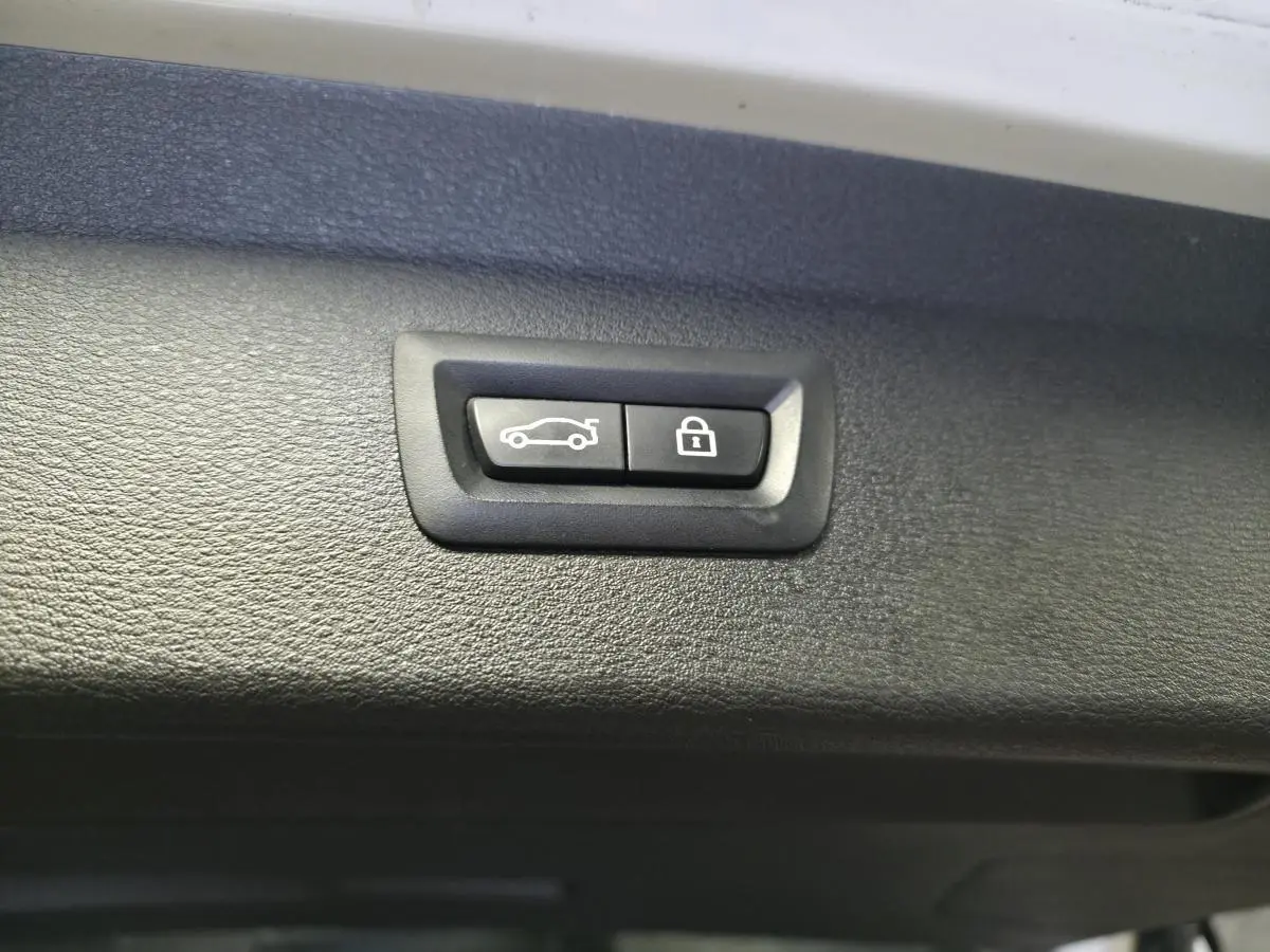Boutons de déverrouillage et fermeture électrique du hayon sur le bord intérieur d’un BMW X1 blanc.