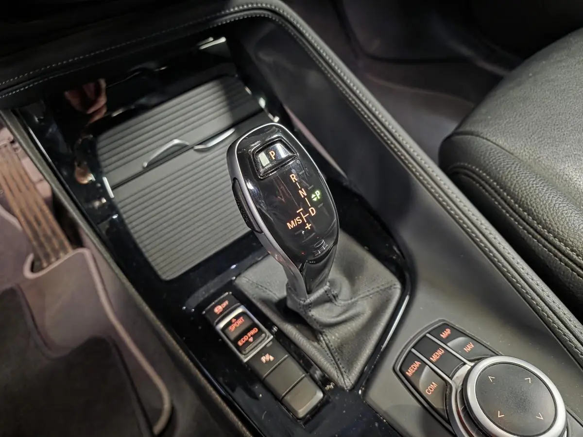 Gros plan sur la console centrale noire du BMW X1 sDrive 18d 2022, avec levier de vitesses automatique et commandes de mode de conduite.
