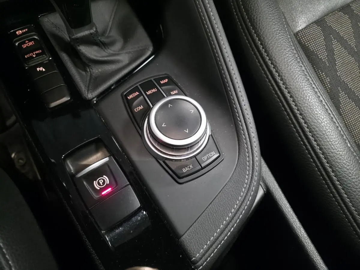 Gros plan sur la console centrale noire avec molette iDrive et commandes de la BMW X1 sDrive 18d BVA Sport xLine 2022.