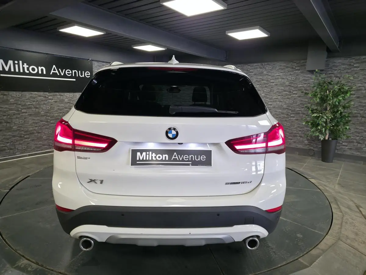 Vue arrière d'un BMW X1 blanc avec feux allumés et double sortie d'échappement chromée dans un showroom.
