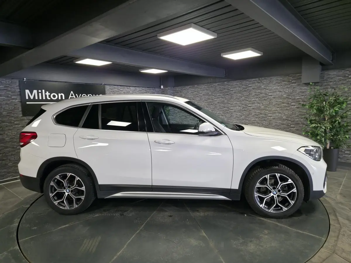 BMW X1 sDrive 18d blanc vue de profil côté gauche, avec jantes alliage 18 pouces et bas de caisse noirs.