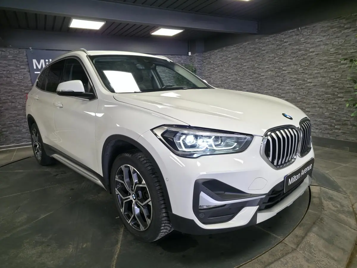 BMW X1 sDrive 18d blanc vue 3/4 avant droit, avec phares LED allumés et jantes alliage 18 pouces style 579.