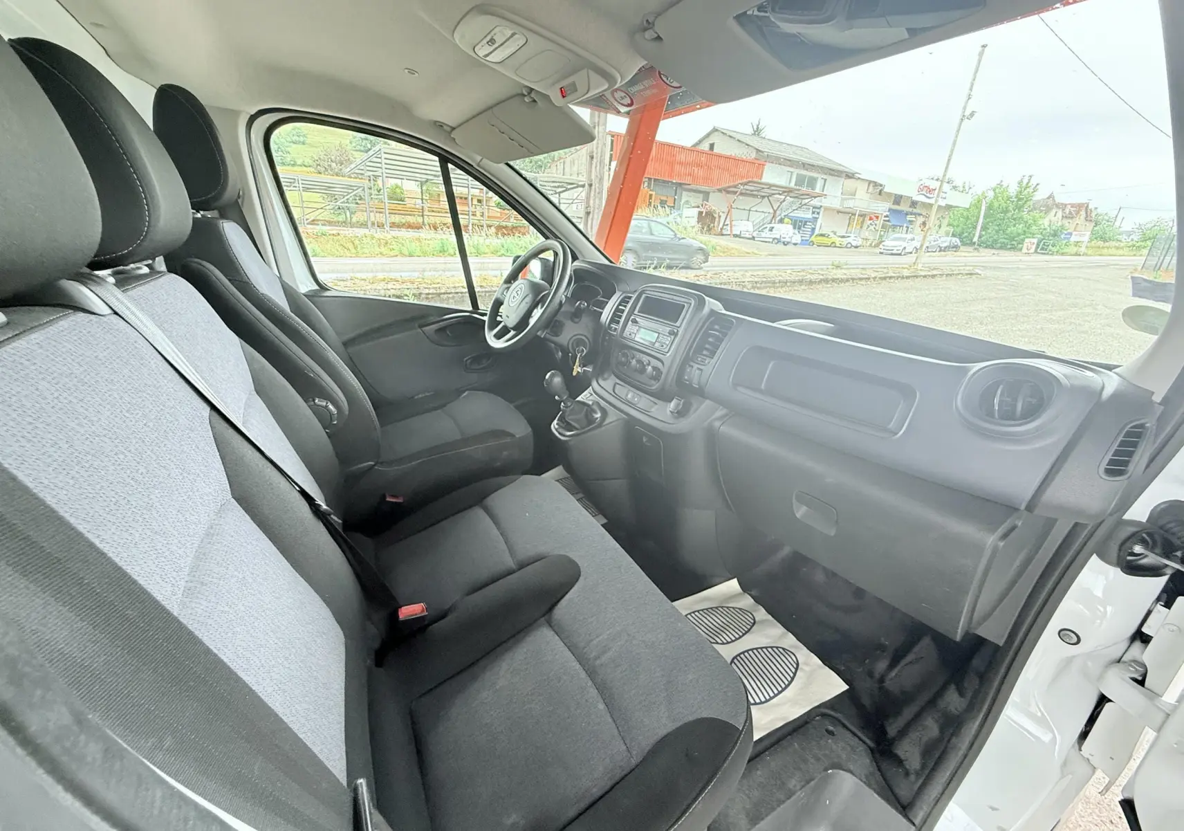 Vue intérieure côté passager de l'Opel Vivaro blanc 2018, montrant les sièges gris et la planche de bord noire.