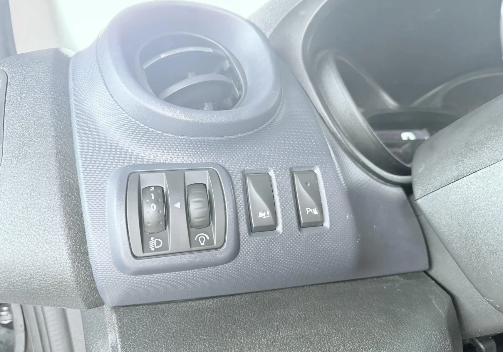 Détail des commandes d'éclairage et d'assistance au stationnement sur tableau de bord gris foncé d'Opel Vivaro blanc.