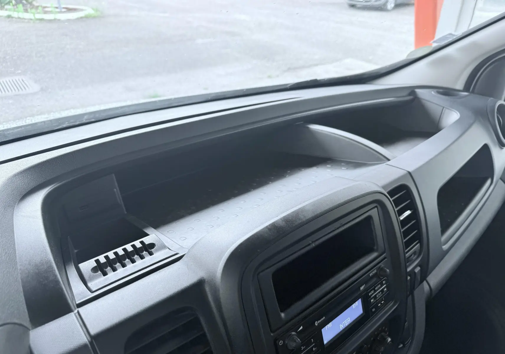 Tableau de bord noir de l'Opel Vivaro 2018 vu de côté, avec console centrale et rangement supérieur visible.