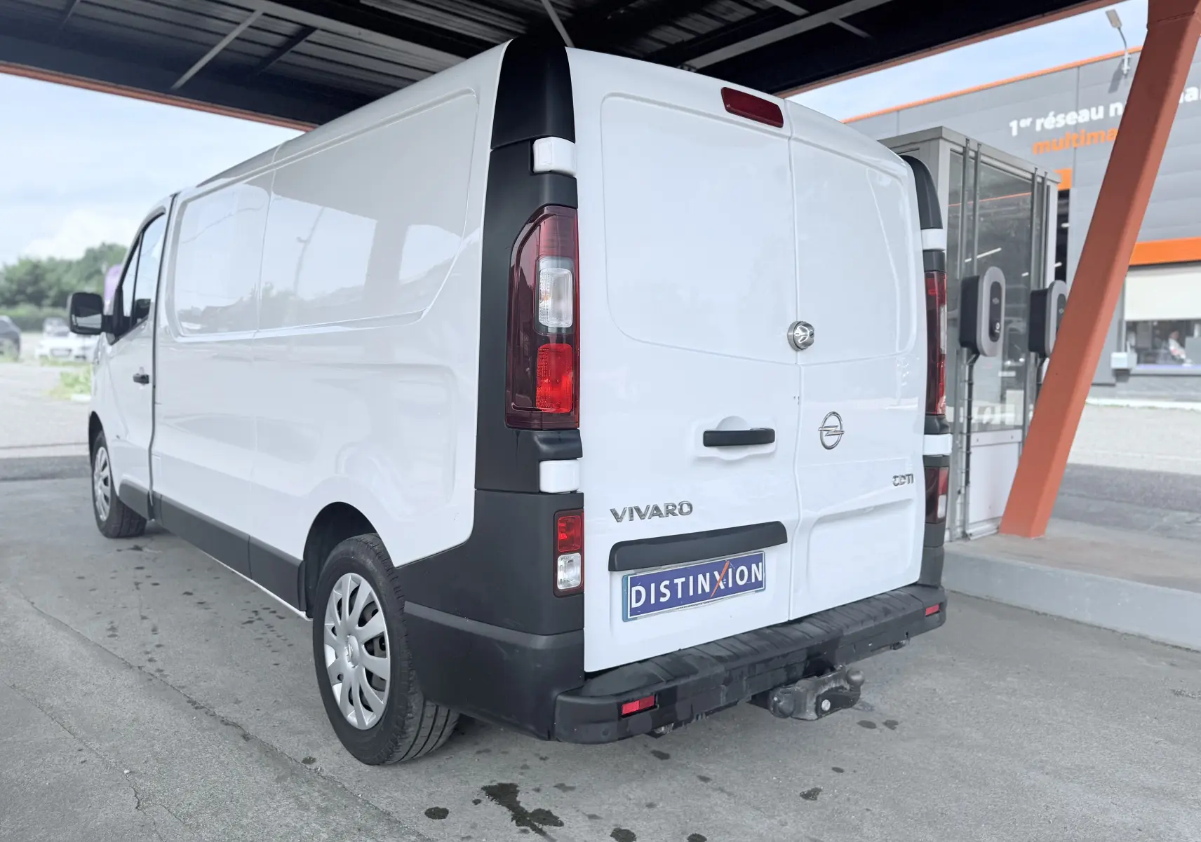 Vue 3/4 arrière droite d’un utilitaire Opel Vivaro blanc avec attelage et pare-chocs noir sous abri.