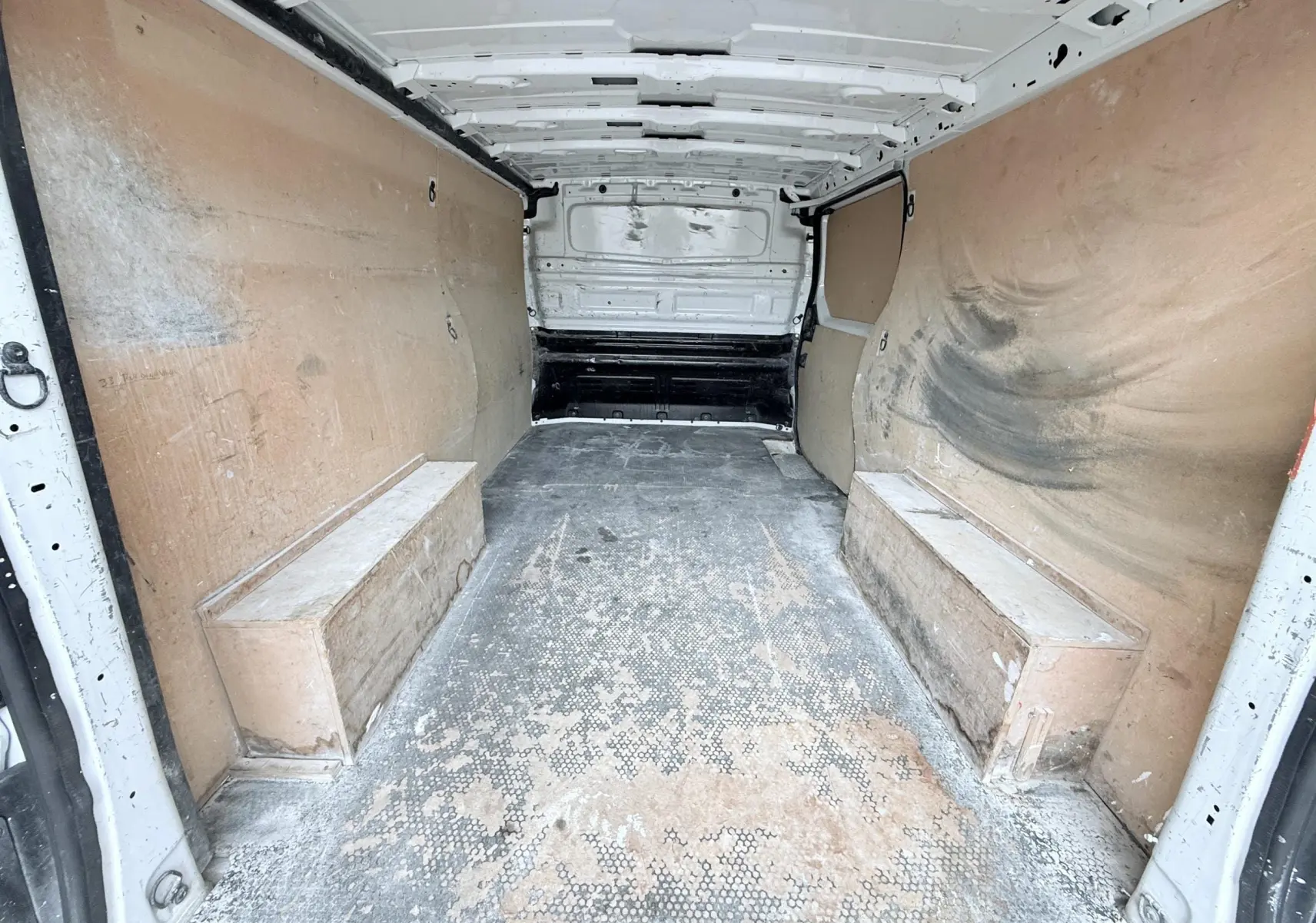 Vue intérieure arrière du fourgon blanc Opel Vivaro 2018, montrant la zone de chargement avec parois en bois usées.