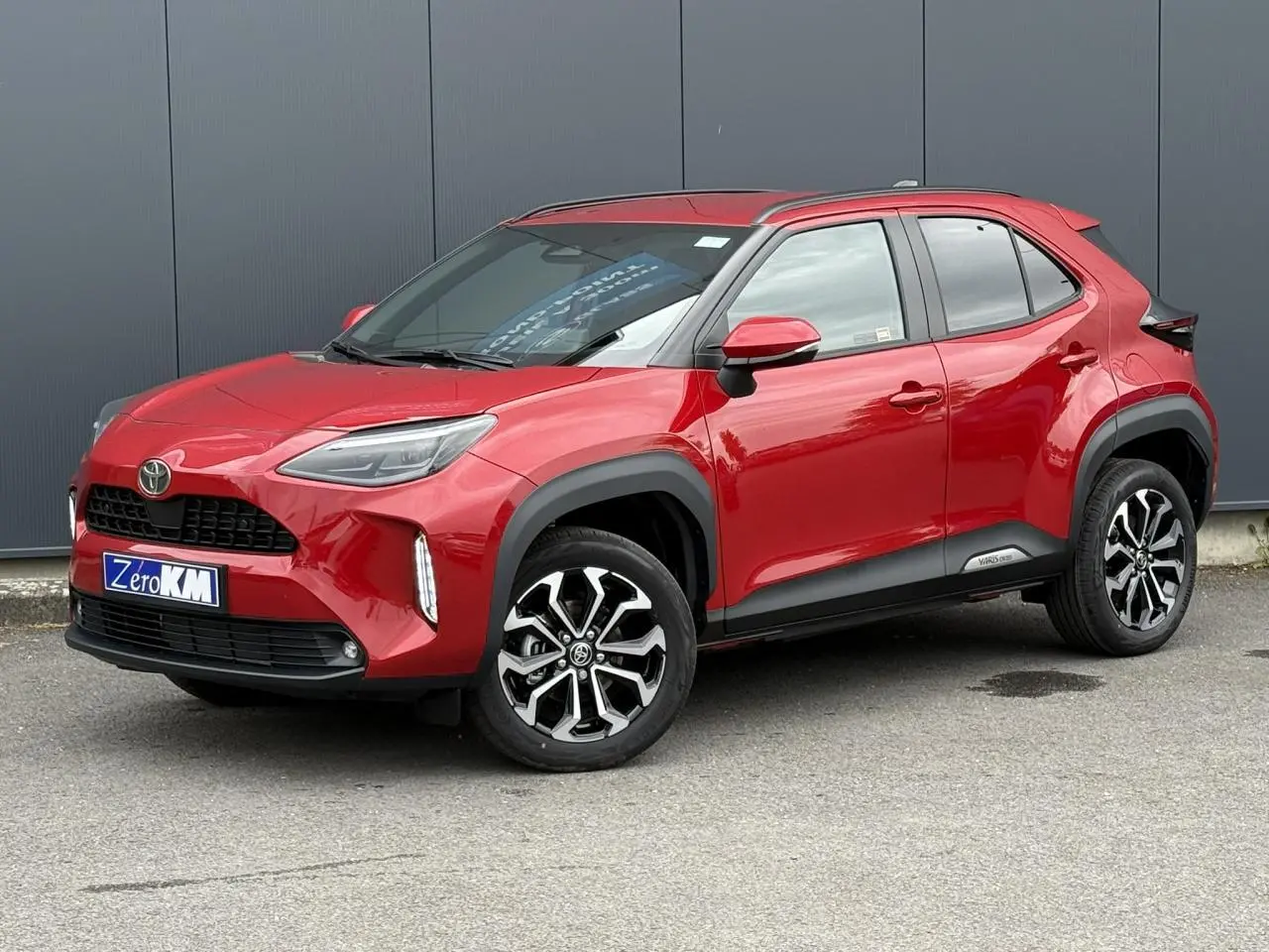 Toyota Yaris Cross rouge intense en 3/4 avant droit, avec jantes alliage et protections noires sur les passages de roue.
