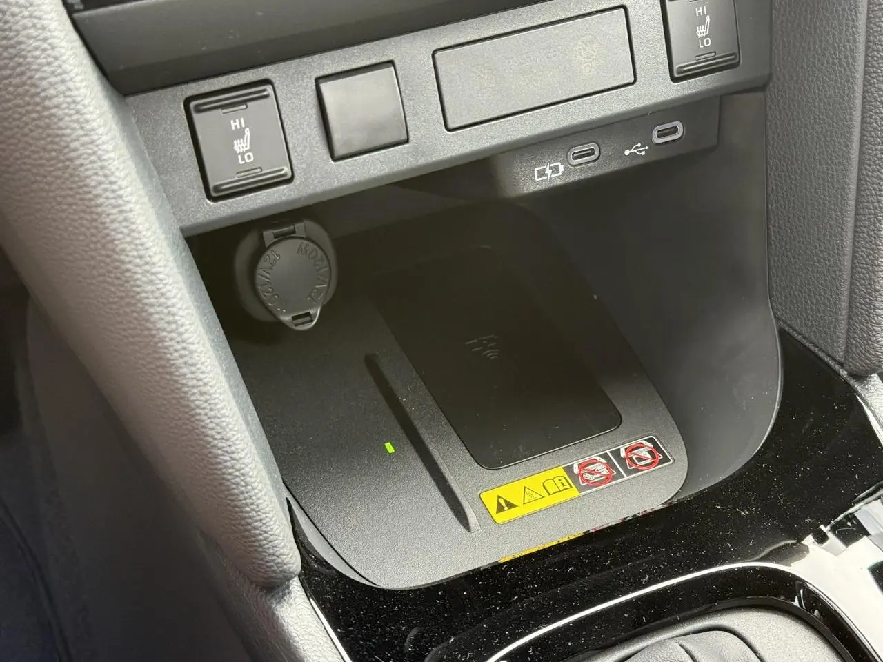 Vue rapprochée de la console centrale de la Toyota Yaris Cross 1.5 Hybrid, montrant le chargeur à induction et commandes sièges chauffants.
