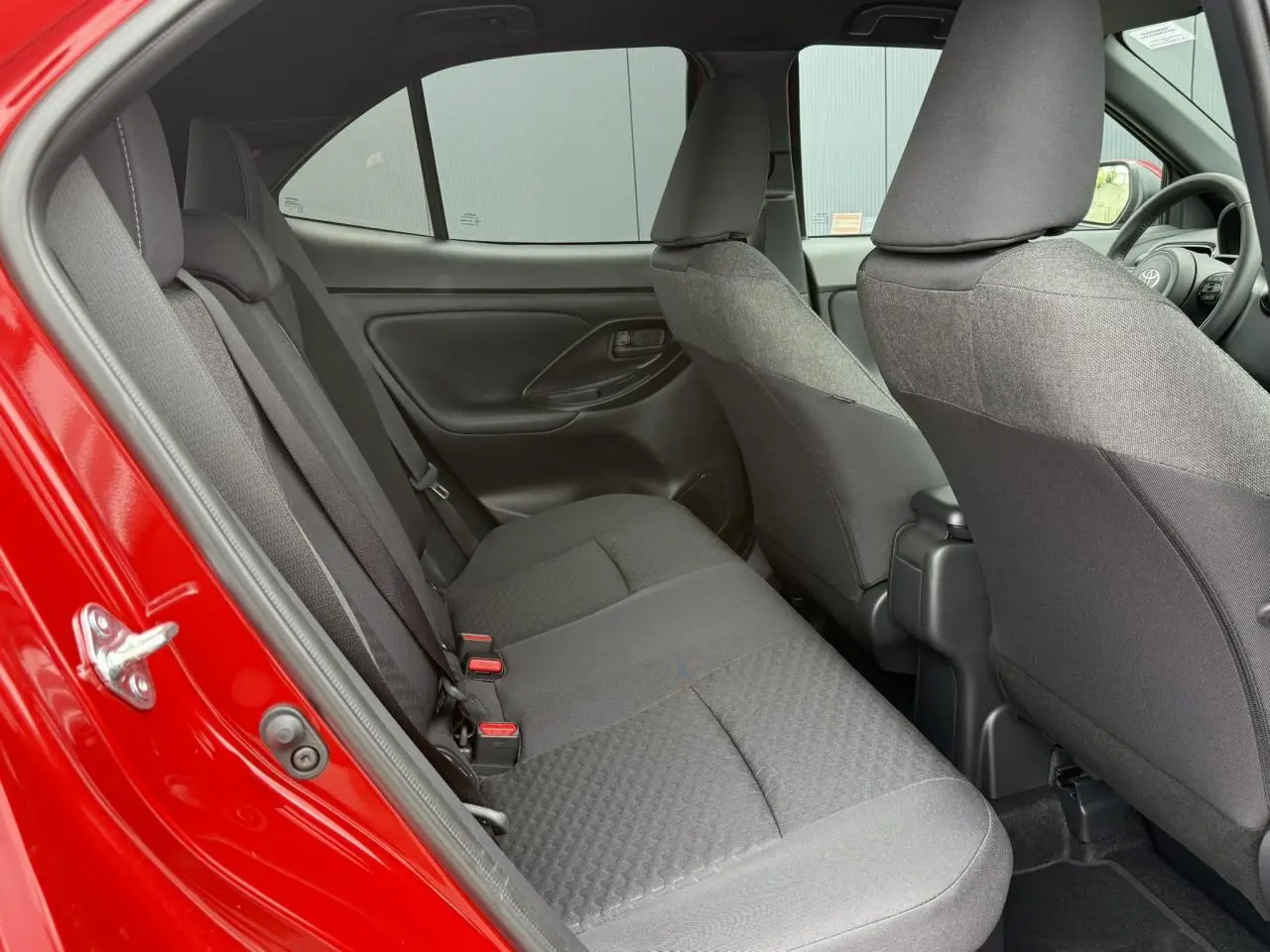 Vue intérieure côté gauche sur les sièges arrière gris d’une Toyota Yaris Cross 1.5 Hybrid rouge intense 2026.