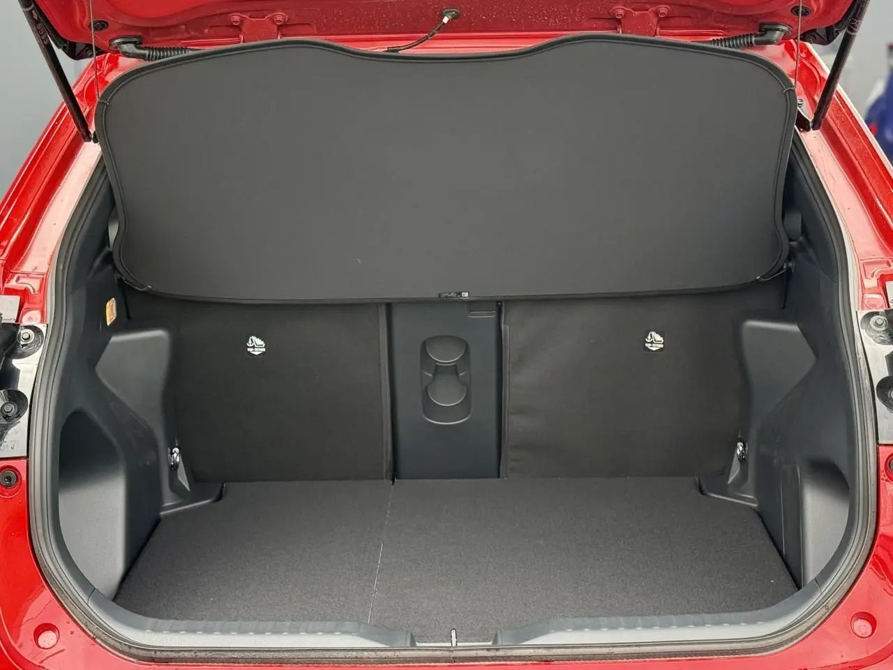 Coffre ouvert vu de l'arrière d'une Toyota Yaris Cross rouge intense, montrant un plancher plat et un cache-bagages noir.