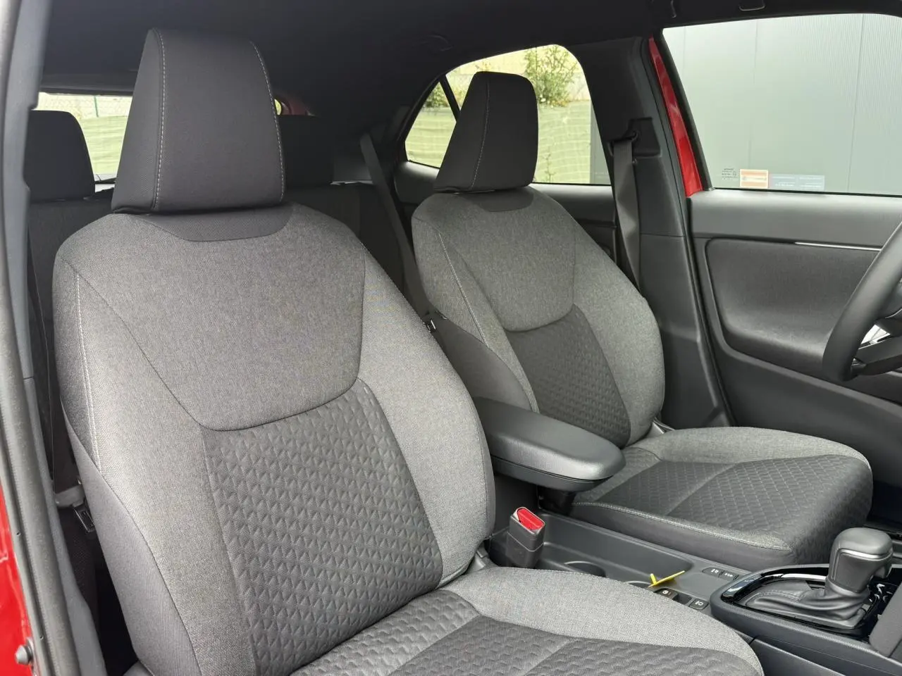 Vue intérieure des sièges avant gris de la Toyota Yaris Cross 1.5 Hybrid 116 Design rouge, avec accoudoir central.