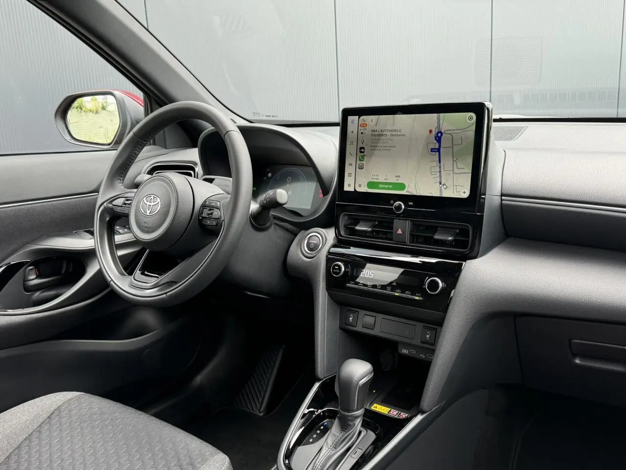 Vue intérieure côté conducteur de la Toyota Yaris Cross rouge intense, avec tableau de bord numérique et écran tactile central.