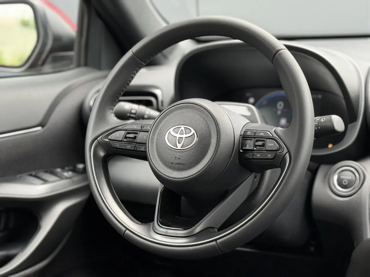 Gros plan sur le volant cuir noir de la Toyota Yaris Cross 2026, avec commandes intégrées et tableau de bord flou en arrière-plan.