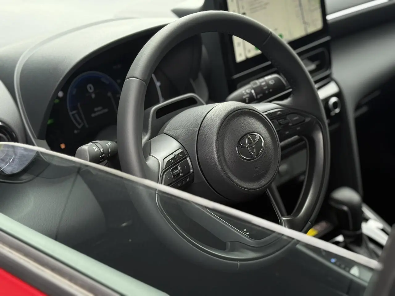 Vue rapprochée du volant cuir noir et du tableau de bord numérique de la Toyota Yaris Cross rouge intense.