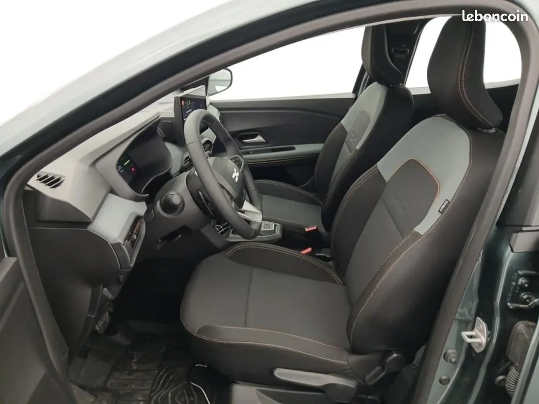 Vue intérieure côté conducteur de la Dacia Sandero verte 2026, sièges noirs avec surpiqûres orange et volant multifonctions.