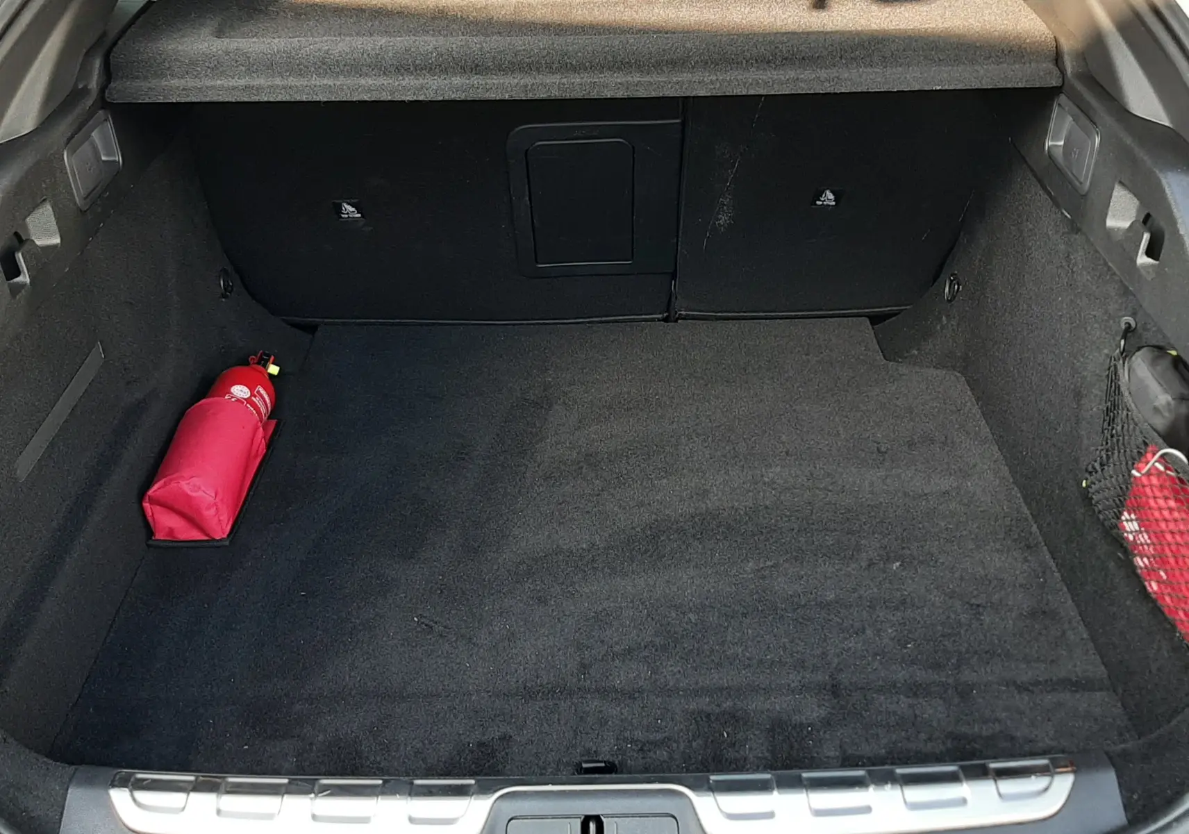 Coffre ouvert vu de l'arrière d'une Peugeot 408 gris selenium, avec un extincteur rouge à gauche et intérieur noir.