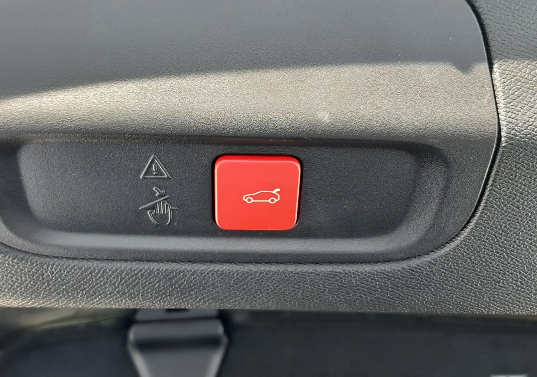 Gros plan sur le bouton rouge d'ouverture électrique du coffre dans l'habitacle d'une Peugeot 408 gris selenium.
