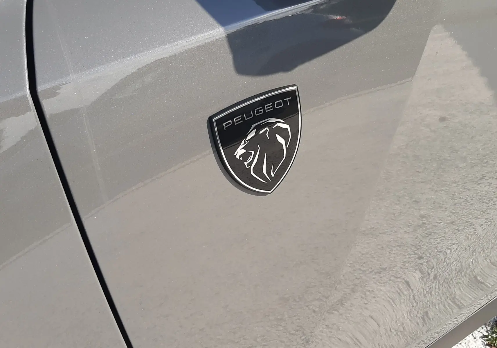 Gros plan sur l'emblème Peugeot noir et argent sur la porte gris selenium côté gauche du véhicule.