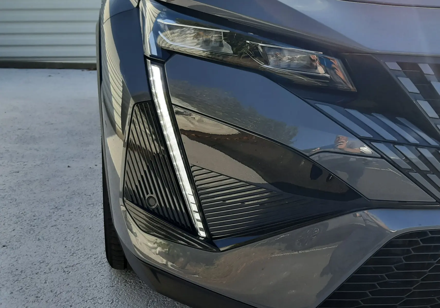 Gros plan sur l'avant droit du Peugeot 408 gris selenium, mettant en valeur le phare LED et la calandre distinctive.