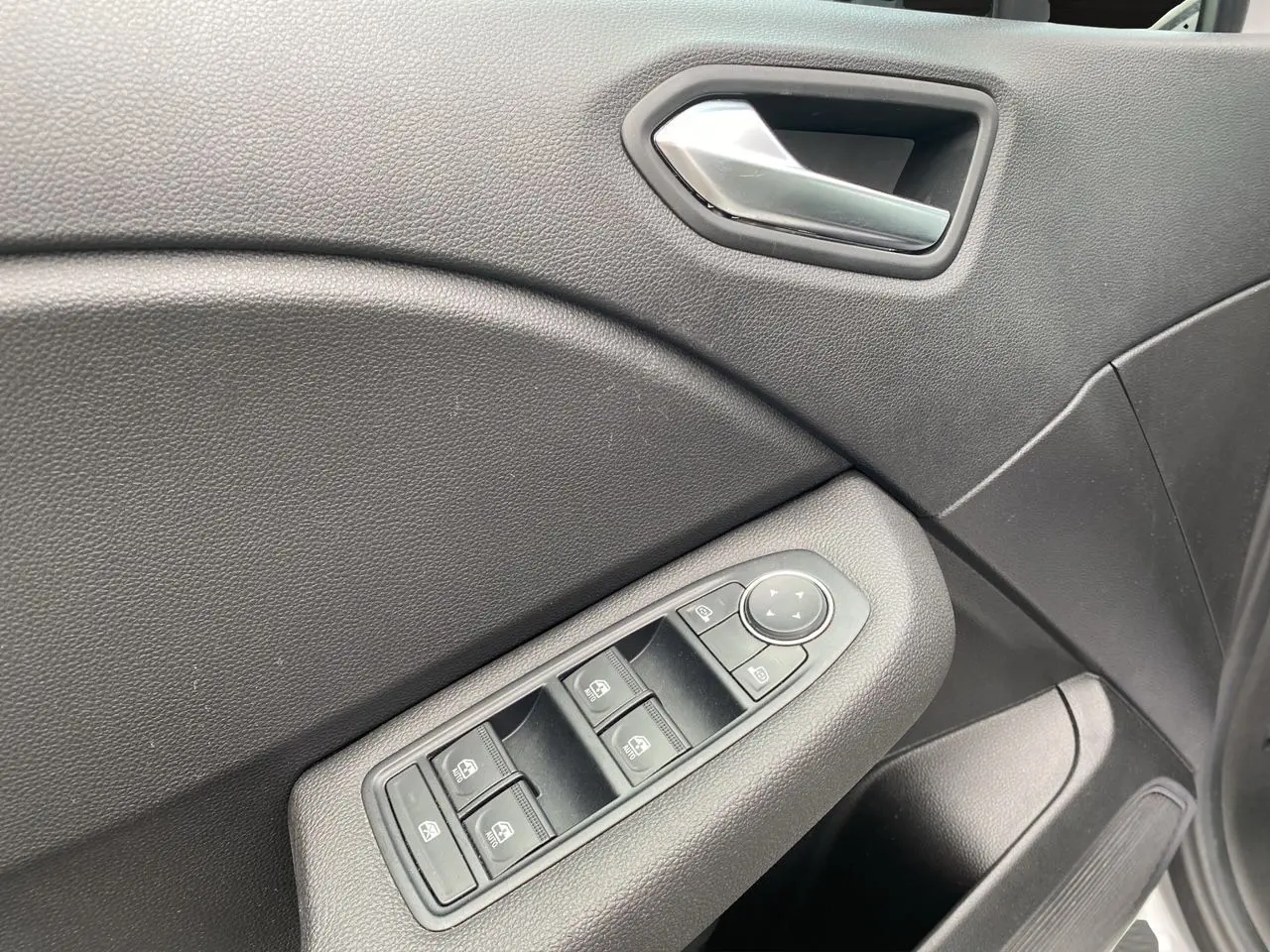 Gros plan sur la commande des vitres électriques côté gauche de la porte intérieure noire d'une Renault Clio V gris Highland.