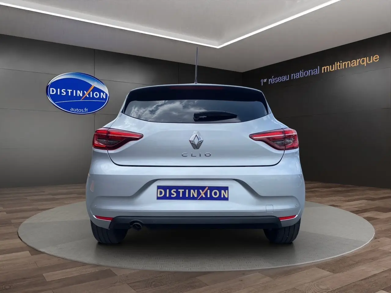 Vue arrière d'une Renault Clio V gris Highland 2023 avec feux LED et plaque Distinxion en showroom.