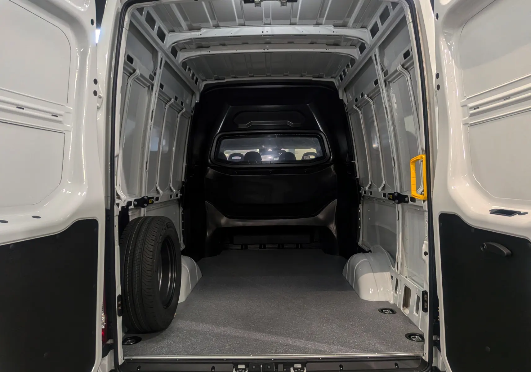 Vue intérieure arrière du fourgon Iveco Daily blanc 2025, montrant l'espace de chargement vide avec une roue de secours à gauche.