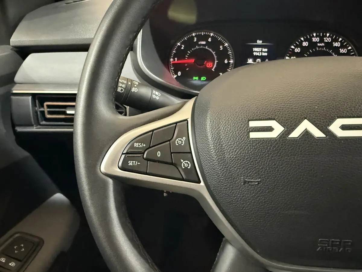 Gros plan sur le volant cuir synthétique de la Dacia Sandero 2024 avec commandes régulateur et tableau de bord éclairé.