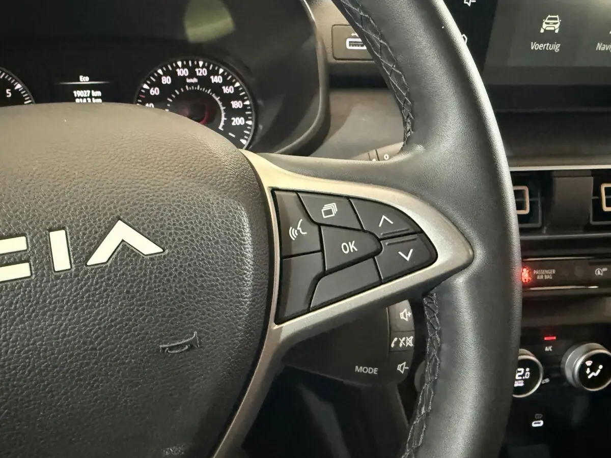 Gros plan sur le volant en cuir noir de la Dacia Sandero 2024, avec commandes multifonctions et tableau de bord partiel visible.
