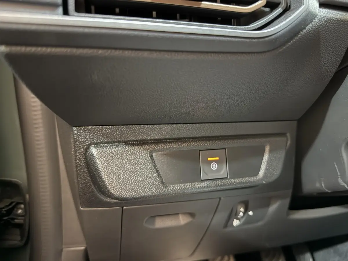 Gros plan sur le bouton de frein à main électrique orange dans l'habitacle noir de la Dacia Sandero 2024.
