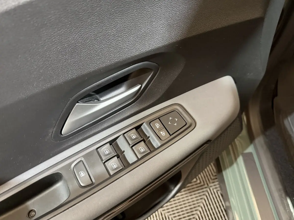 Vue rapprochée de la porte côté conducteur d’une Dacia Sandero 2024 verte, montrant les commandes des vitres électriques.