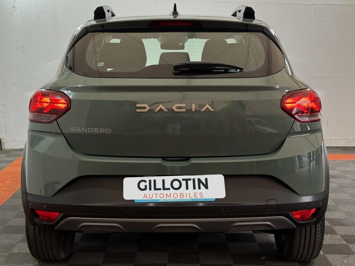 Vue arrière d'une Dacia Sandero Extreme+ TCe 110 2024 en vert avec feux LED allumés et barres de toit grises.