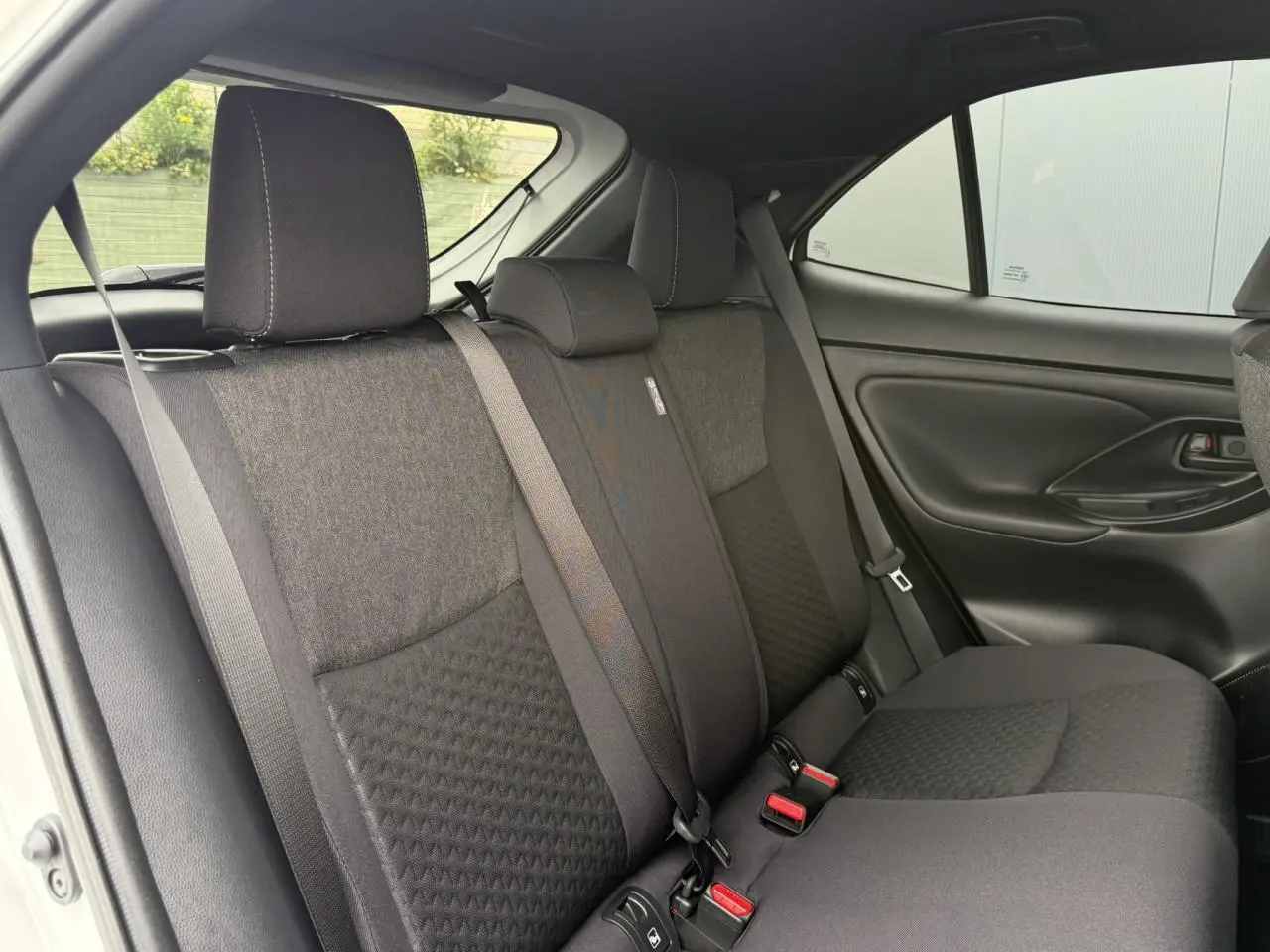 Vue intérieure des sièges arrière noirs du Toyota Yaris Cross 1.5 Hybrid 116 Design avec ceinture de sécurité et porte latéral visible.