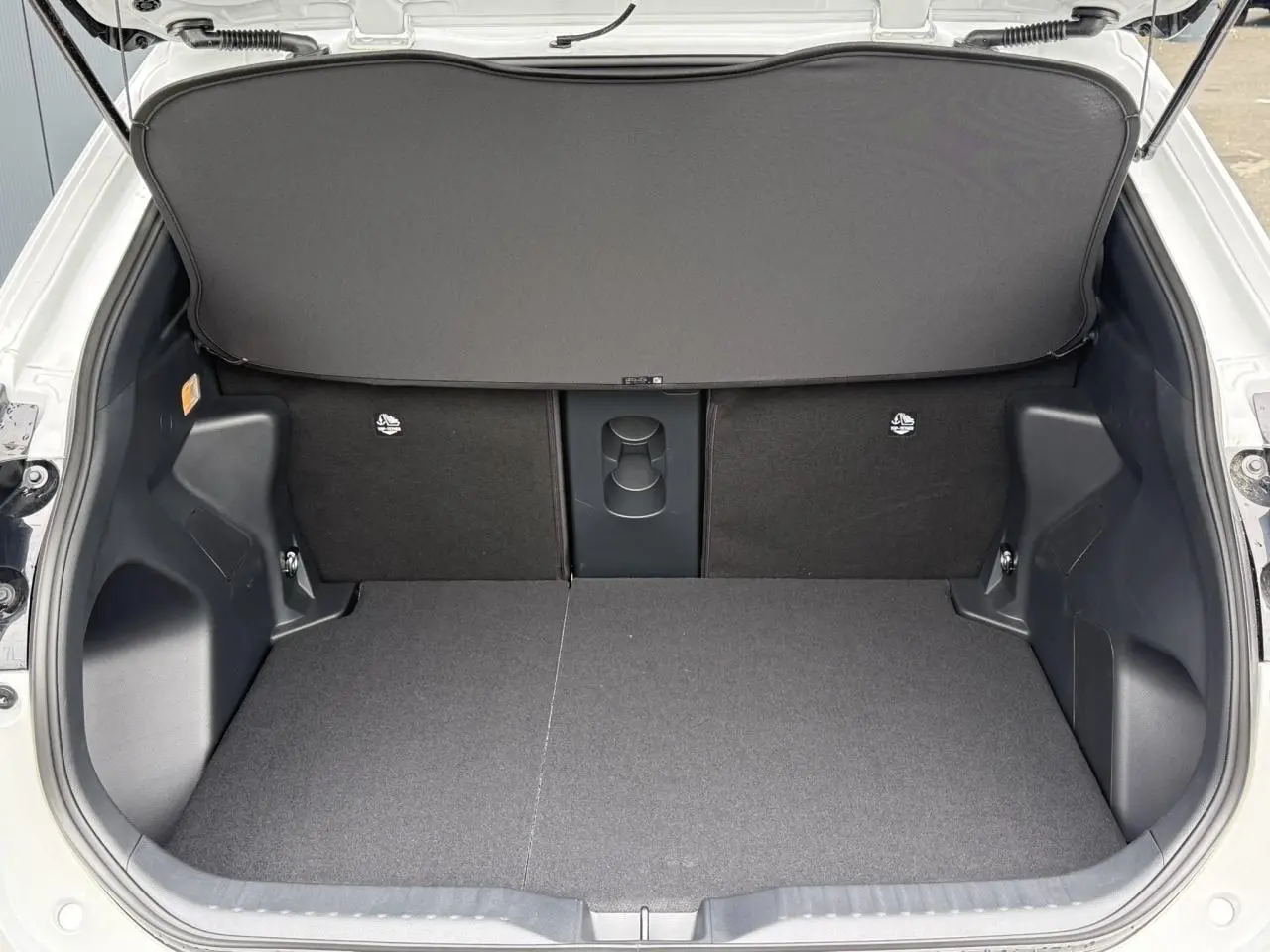 Coffre ouvert vu de l'arrière d'une Toyota Yaris Cross blanc lunaire avec plancher plat et sièges arrière rabattables.