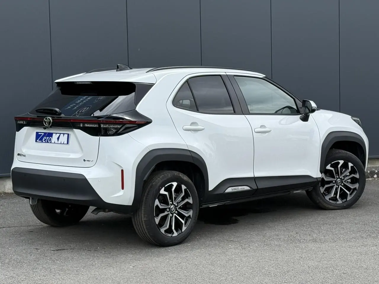 Vue 3/4 arrière droite de la Toyota Yaris Cross 1.5 Hybrid blanche avec toit noir et jantes alliage bicolores.