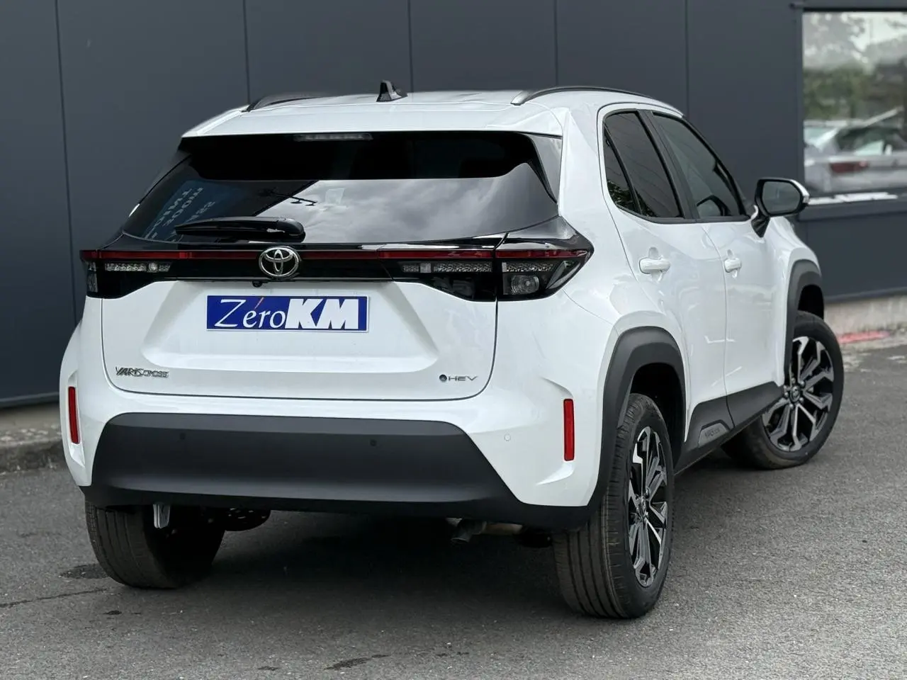 Vue 3/4 arrière droite d'une Toyota Yaris Cross 1.5 Hybrid blanc lunaire avec feux arrière full LED et vitres surteintées.