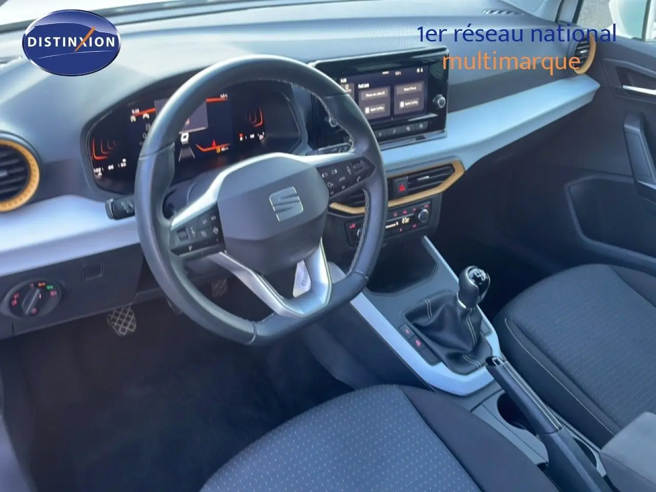 Vue intérieure côté conducteur du tableau de bord et volant du SEAT Arona blanc, avec sellerie tissu noire et console centrale.