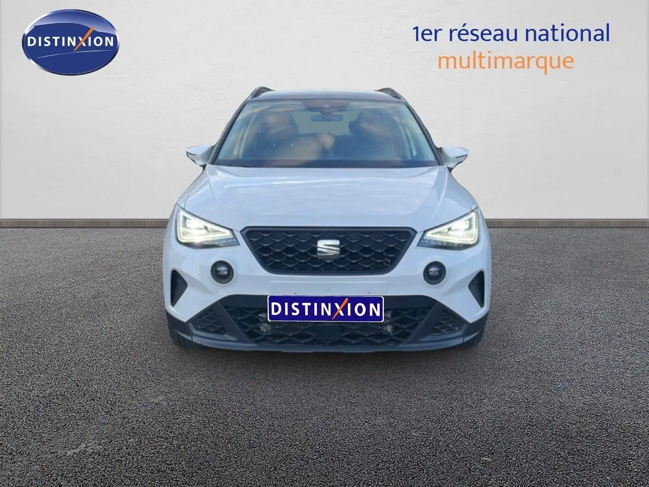 Vue frontale du SEAT Arona blanc avec toit gris, phares LED allumés et calandre noire distinctive.