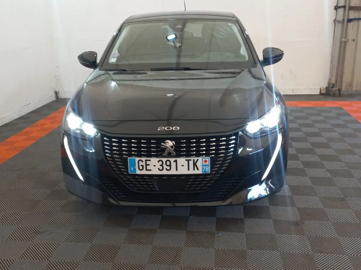 Peugeot 208 noire vue de face, phares LED allumés et signature lumineuse en forme de griffes visibles.