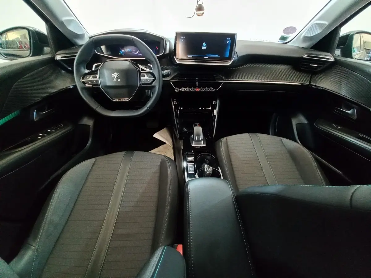 Vue intérieure avant de la Peugeot 208 noire, avec tableau de bord digital et écran tactile central lumineux.