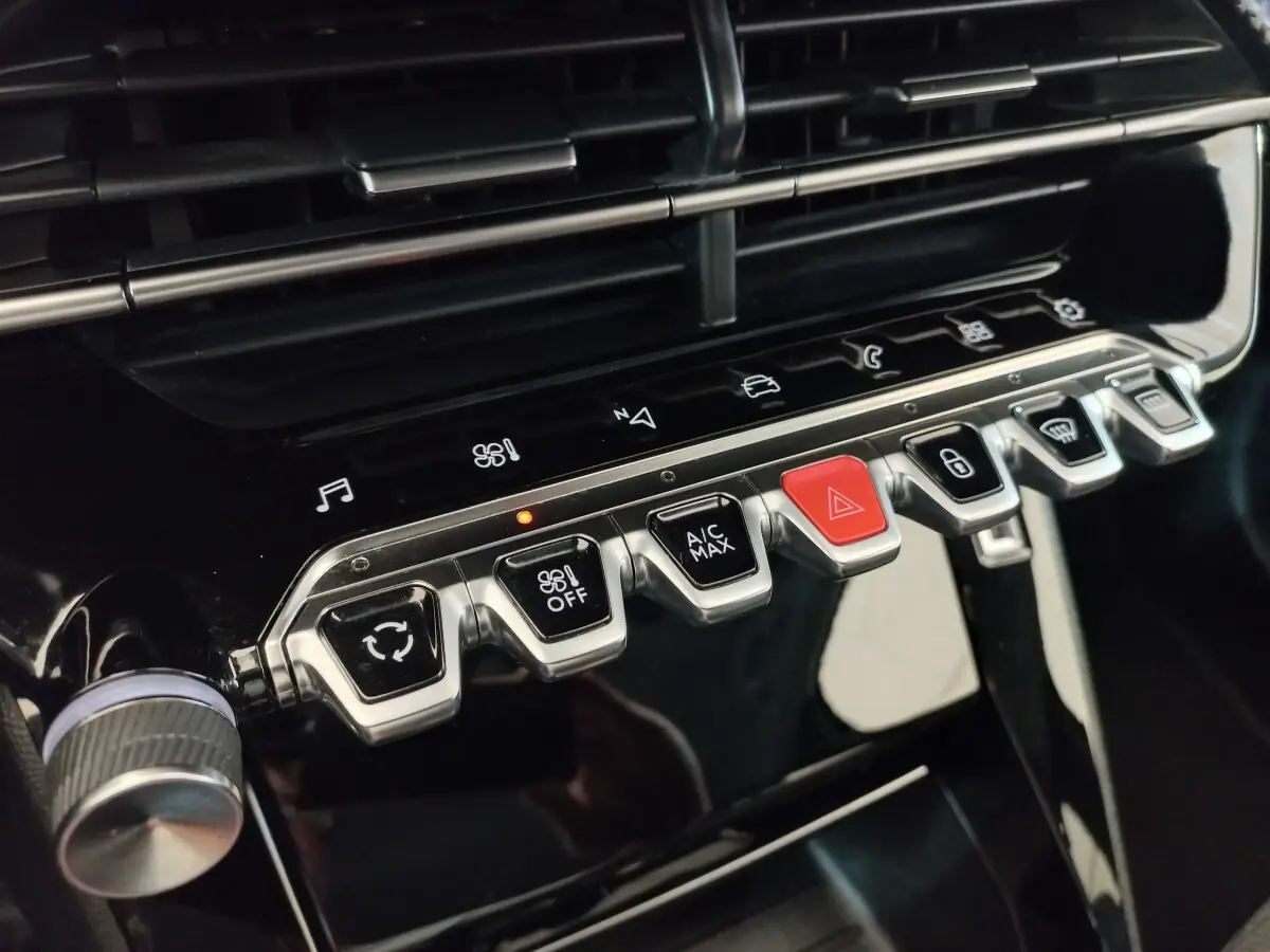 Gros plan sur les commandes centrales noires et chromées du tableau de bord de la Peugeot 208 PureTech 100 noir, avec bouton rouge d’alerte.