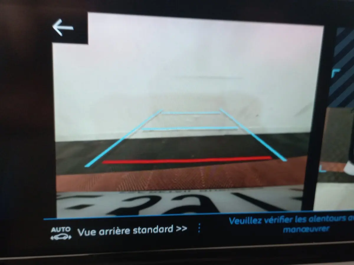 Affichage de la caméra de recul de la Peugeot 208 noire, avec lignes de guidage bleues et rouges visibles à l'écran.