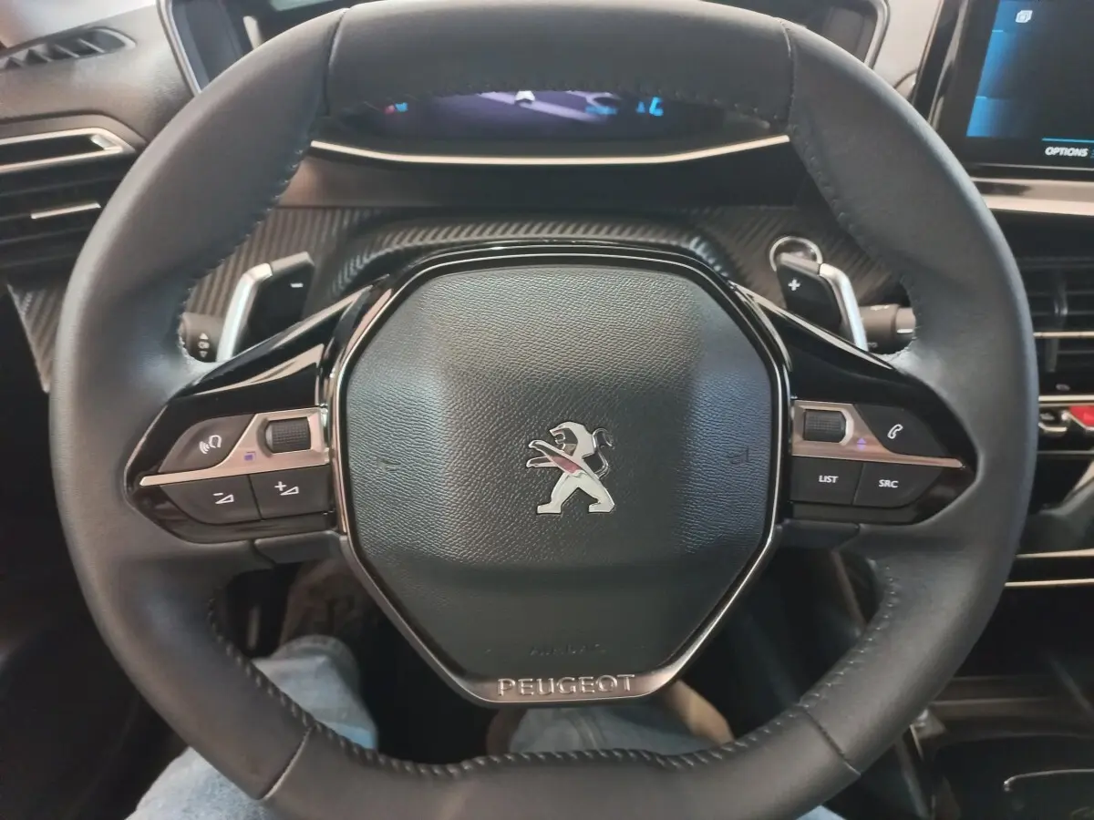 Vue rapprochée du volant cuir noir de la Peugeot 208 2022 avec commandes multifonctions et logo central.