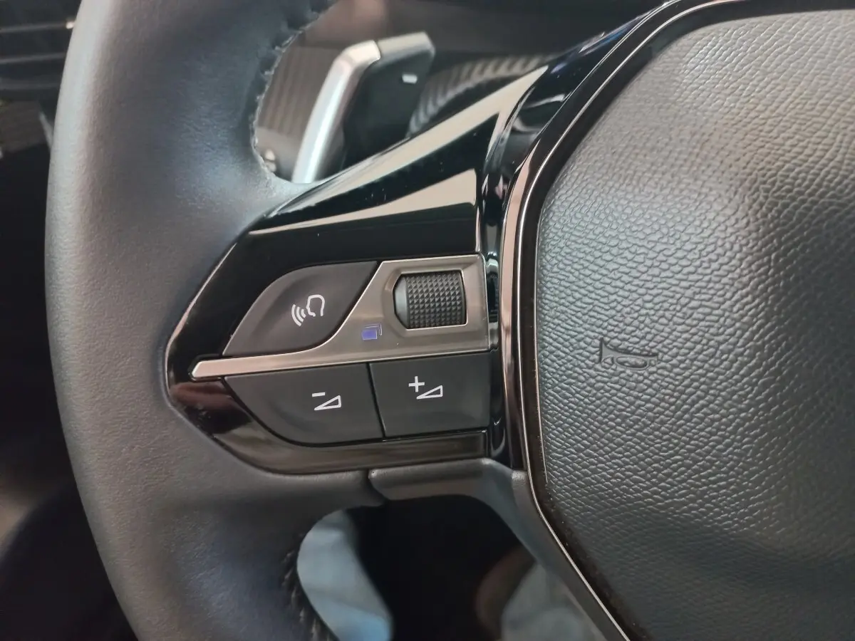 Gros plan sur les commandes gauche du volant cuir noir de la Peugeot 208 PureTech 100 Allure Pack 2022.
