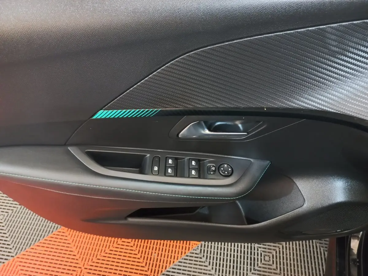 Vue intérieure côté gauche de la porte d’une Peugeot 208 noire, avec commandes des vitres et poignée intégrée.
