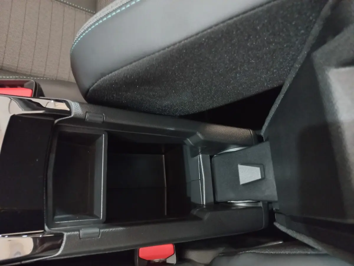 Vue rapprochée de la console centrale noire ouverte de la Peugeot 208 PureTech 100 Allure Pack, montrant le rangement intérieur.