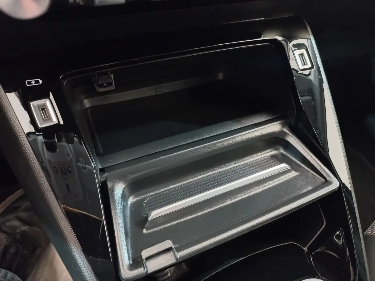 Gros plan intérieur sur la console centrale noire brillante avec compartiment ouvert et ports USB visibles.